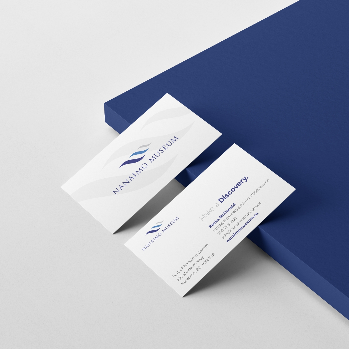 A pair of Nanaimo Museum business cards showcases both sides of the design. The front prominently features the Nanaimo Museum logo in brand colors of grey, blue, and dark blue. On the back, the logo is on the left with the museum's address beneath it, while the contact information is placed neatly on the right. The cards maintain a clean, minimalist aesthetic, evoking professionalism and a polished brand identity.