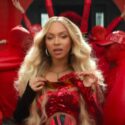Beyoncé in a red sequined dress at the forefront of a vibrant scene with dancers in red outfits.